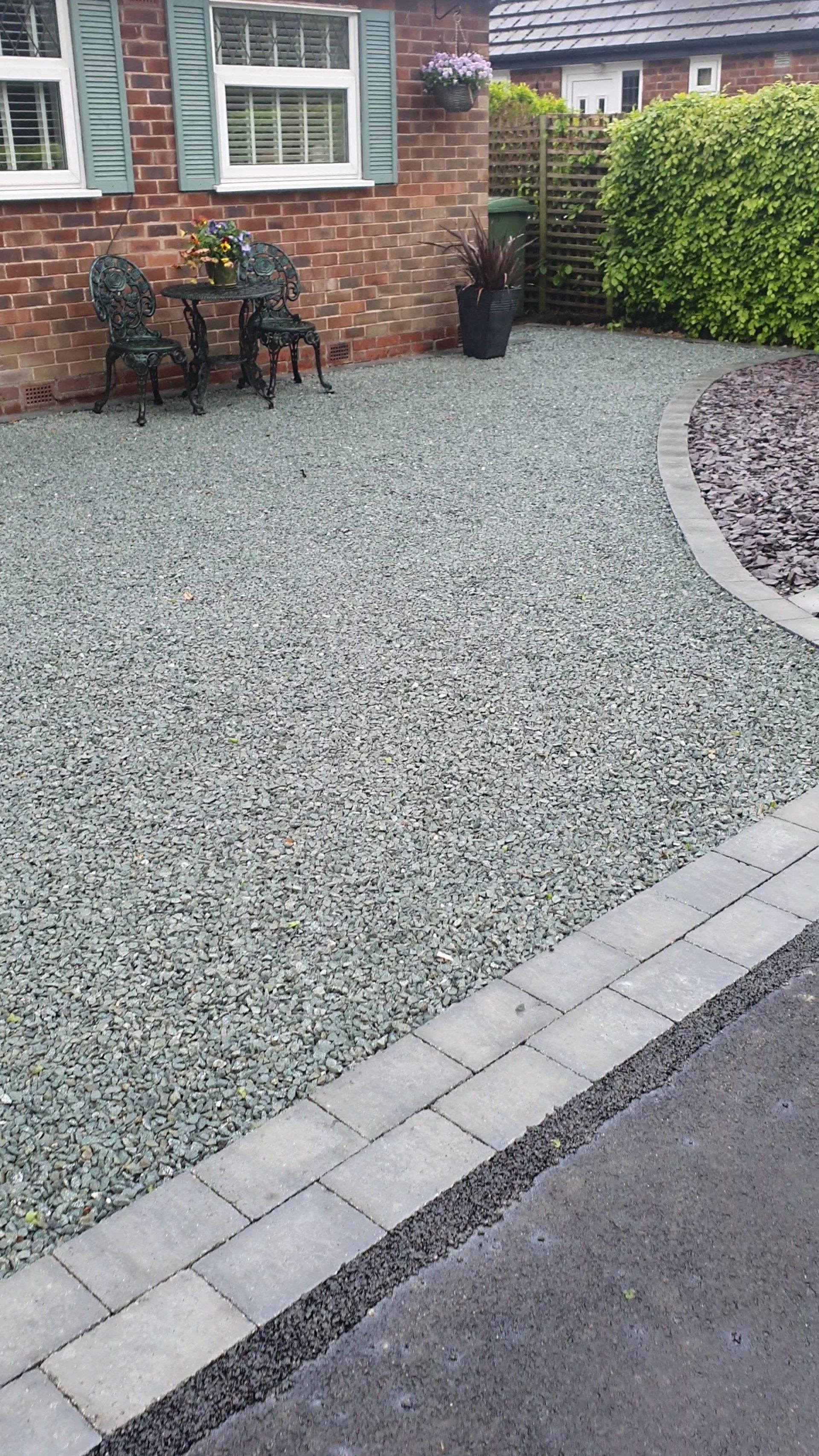 Gravel pathway leading to a brick house with chairs and a small table on the gravel.
