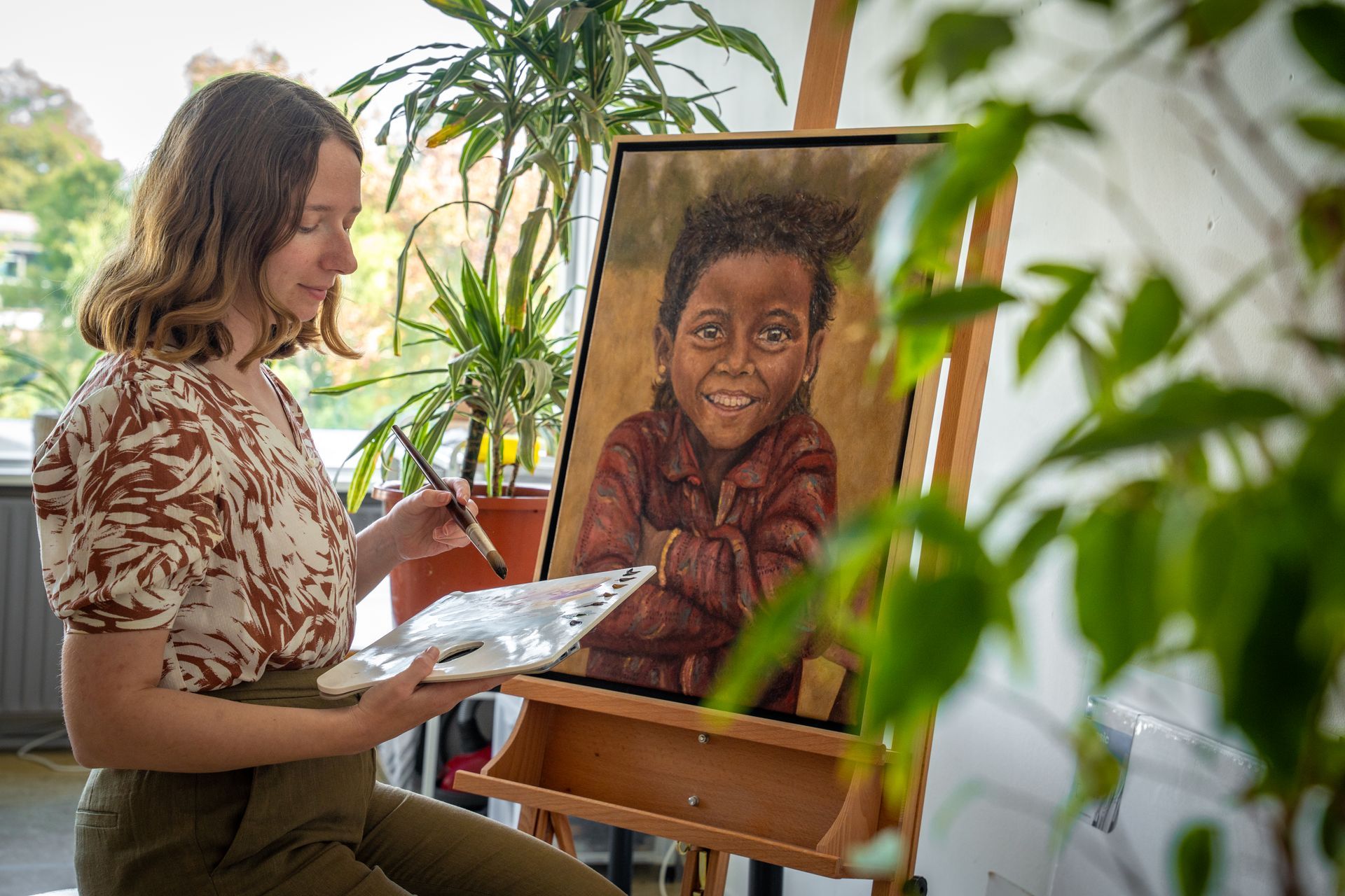 Kunstenaar schildert een portret van een lachend kind op een schildersezel in een lichte studio.