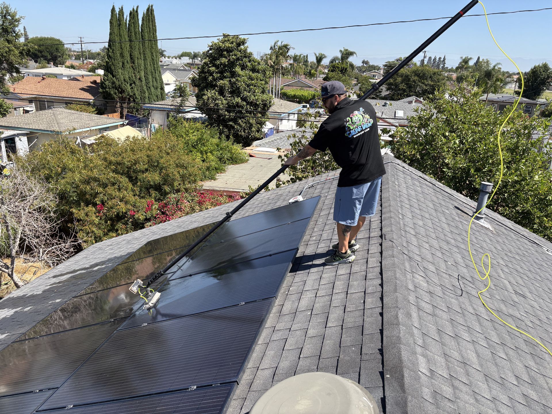 Worker standing on a shingled roof, inspecting or repairing solar panels in a suburban neighborhood
