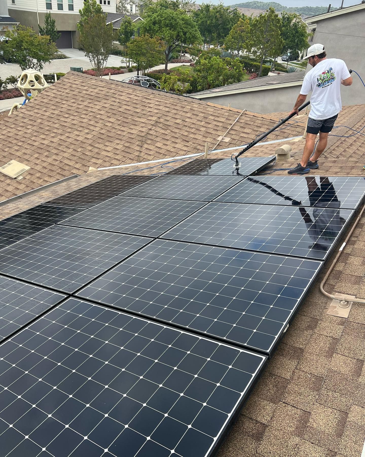 Worker installing black solar panels on a rooftop beside a gravel section