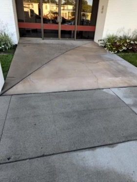 Concrete ramp leading to glass entrance doors, with a sloped transition over the walkway