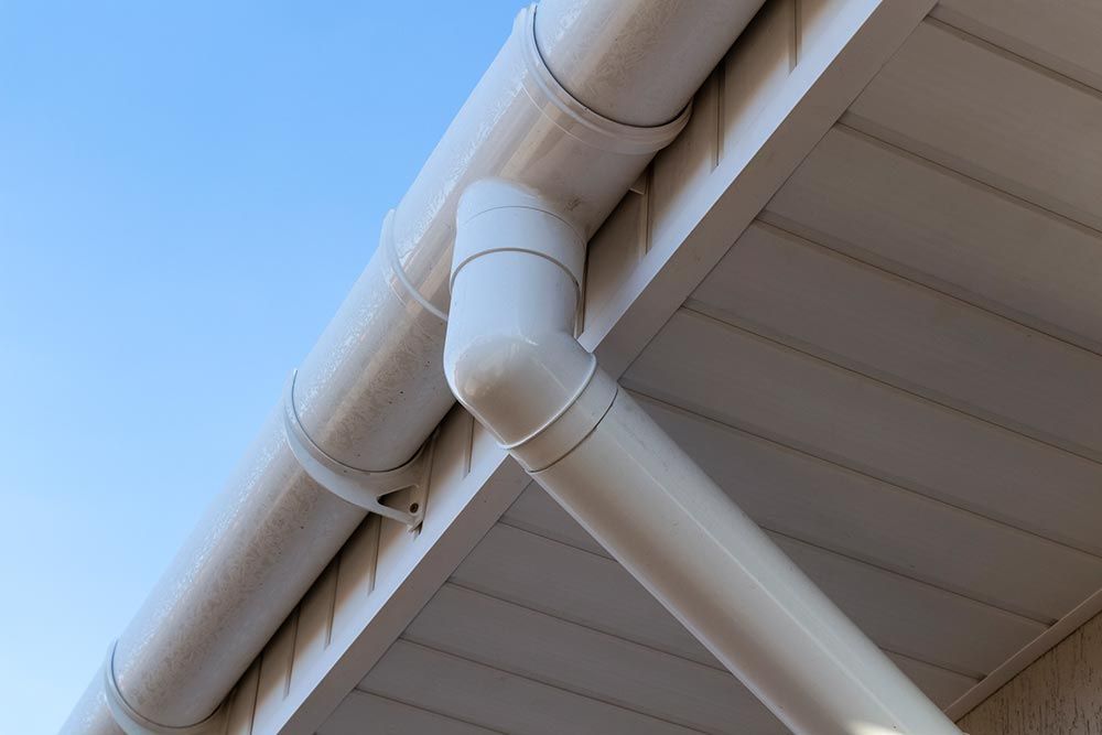 White house gutter and downspout corner against a blue sky