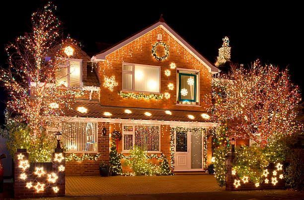 House covered in warm Christmas lights and wreaths at night, with lit trees and glowing front yard decorations