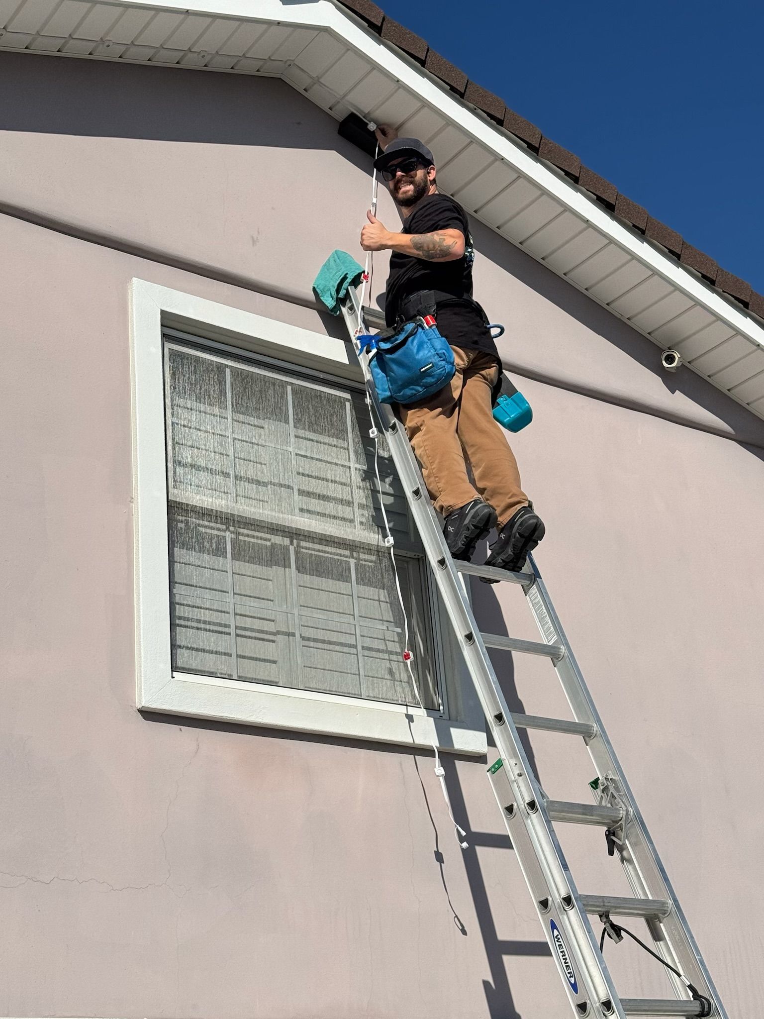 Person on a ladder near a house roof, assisting another climber below a window.