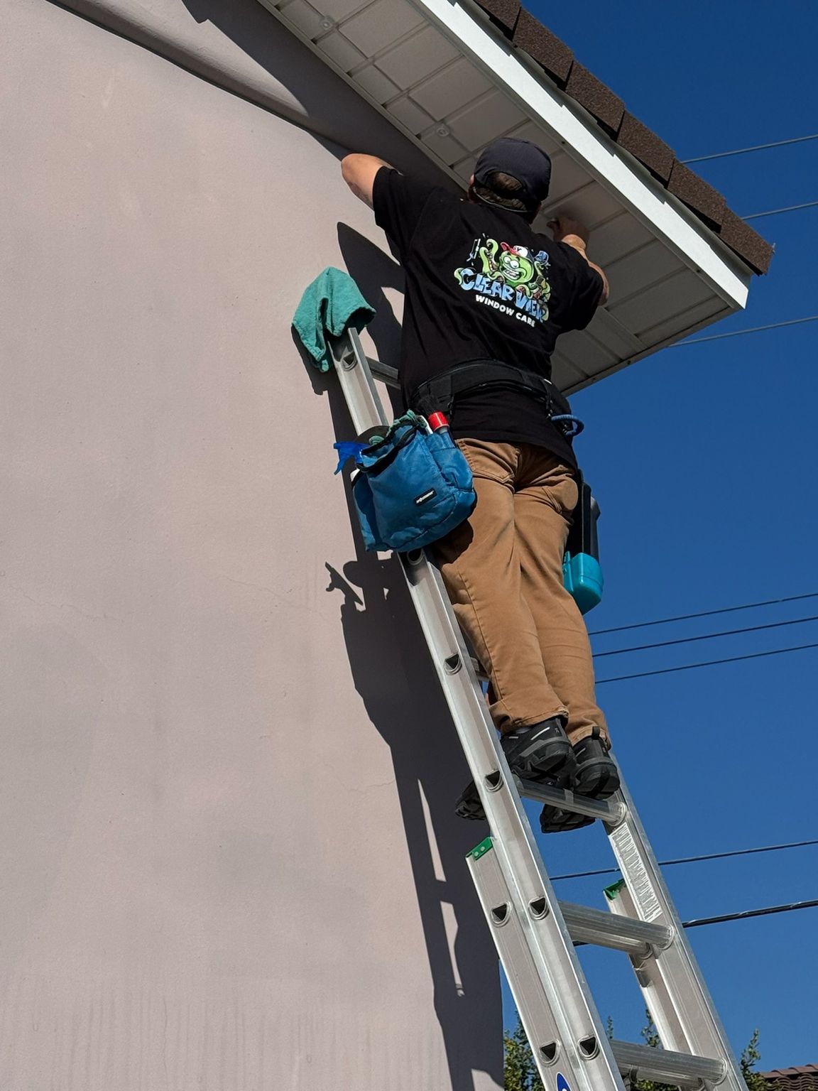 Worker on a ladder painting the side of a house near the roofline.