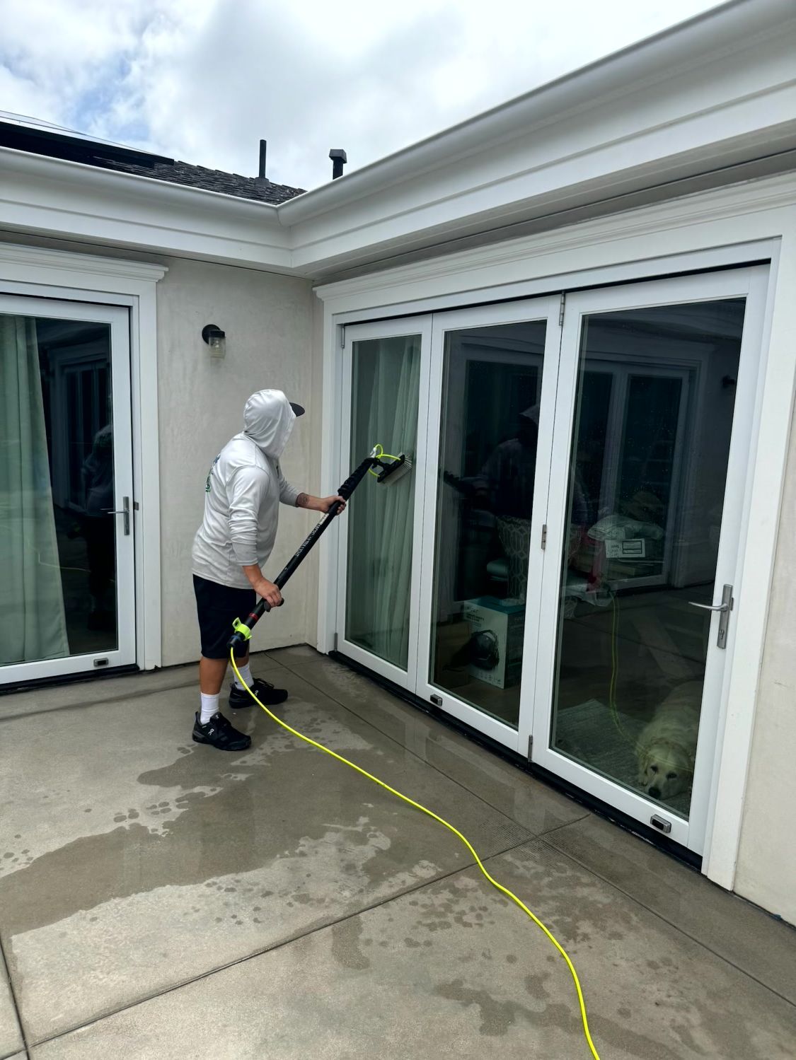 Worker pressure-washing patio beside white sliding glass doors with a hose and wand