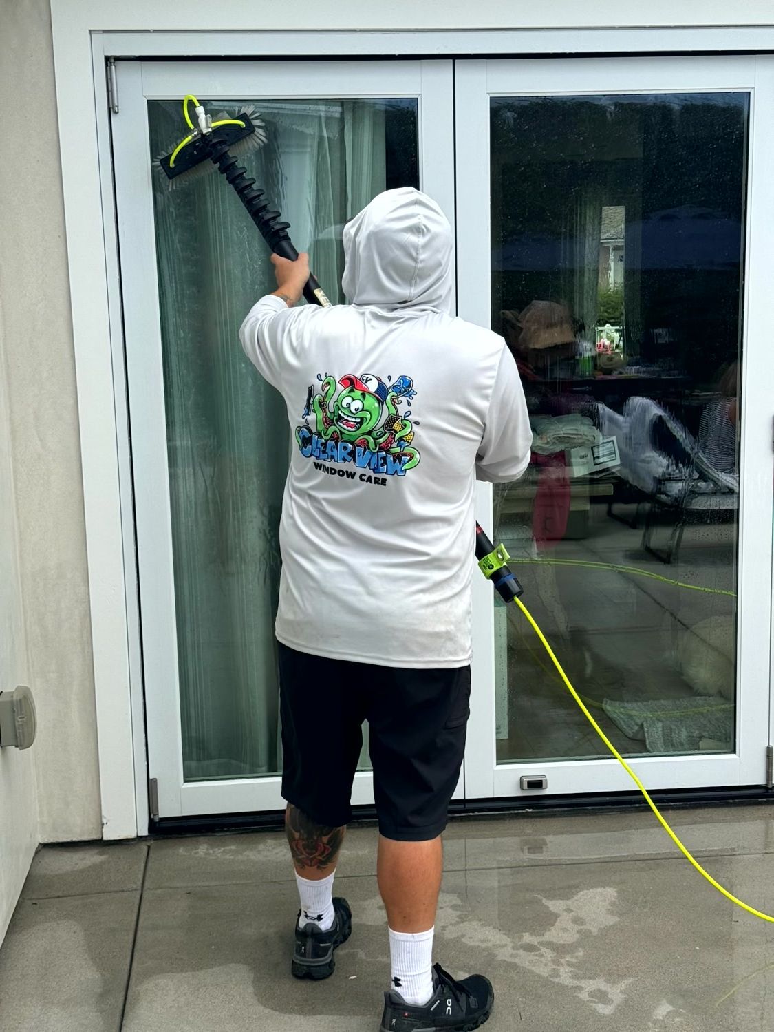 Person cleaning a glass door with a squeegee and extension pole indoors