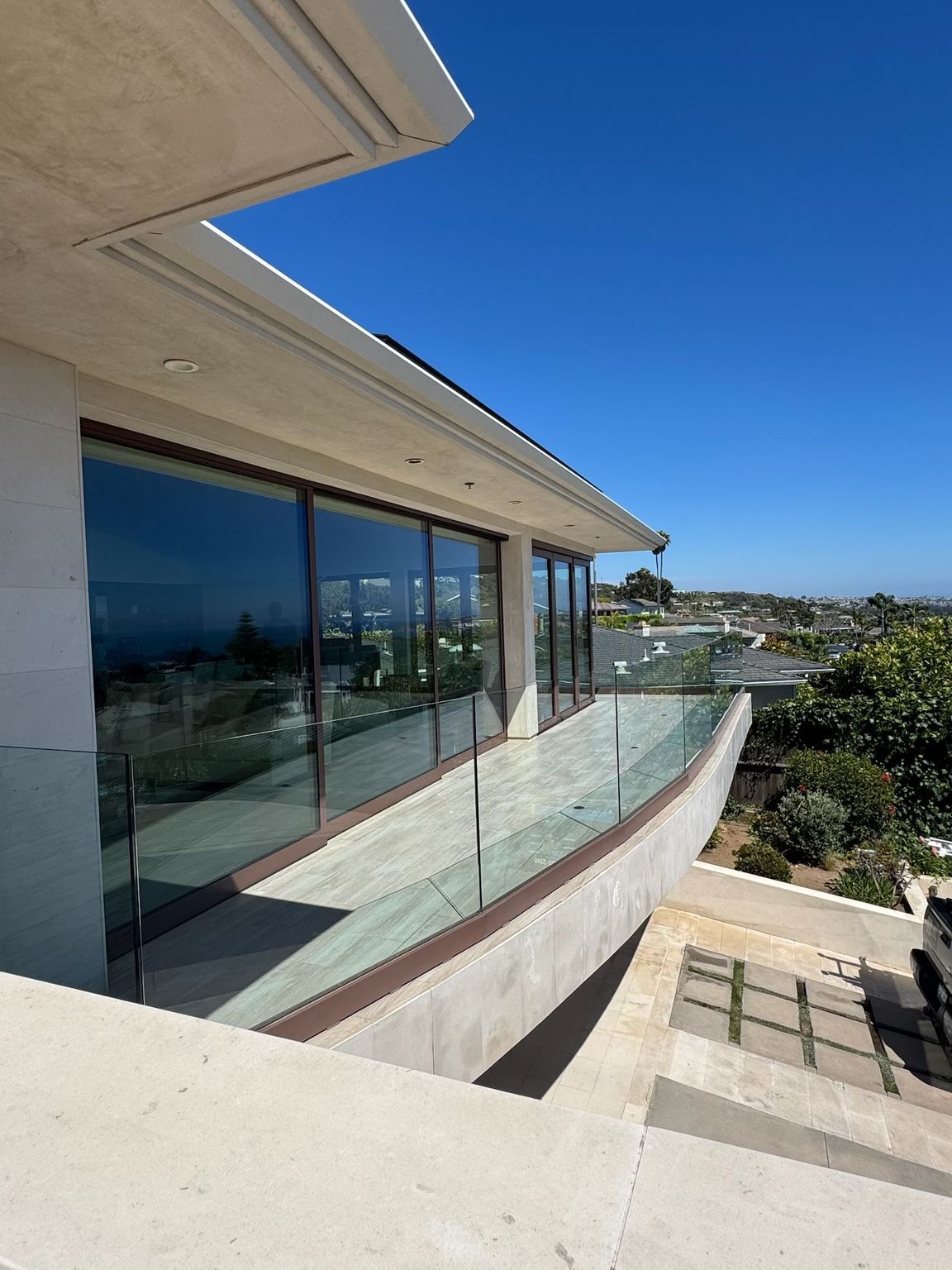Modern house balcony with glass railing overlooking a sunny hillside and blue sky