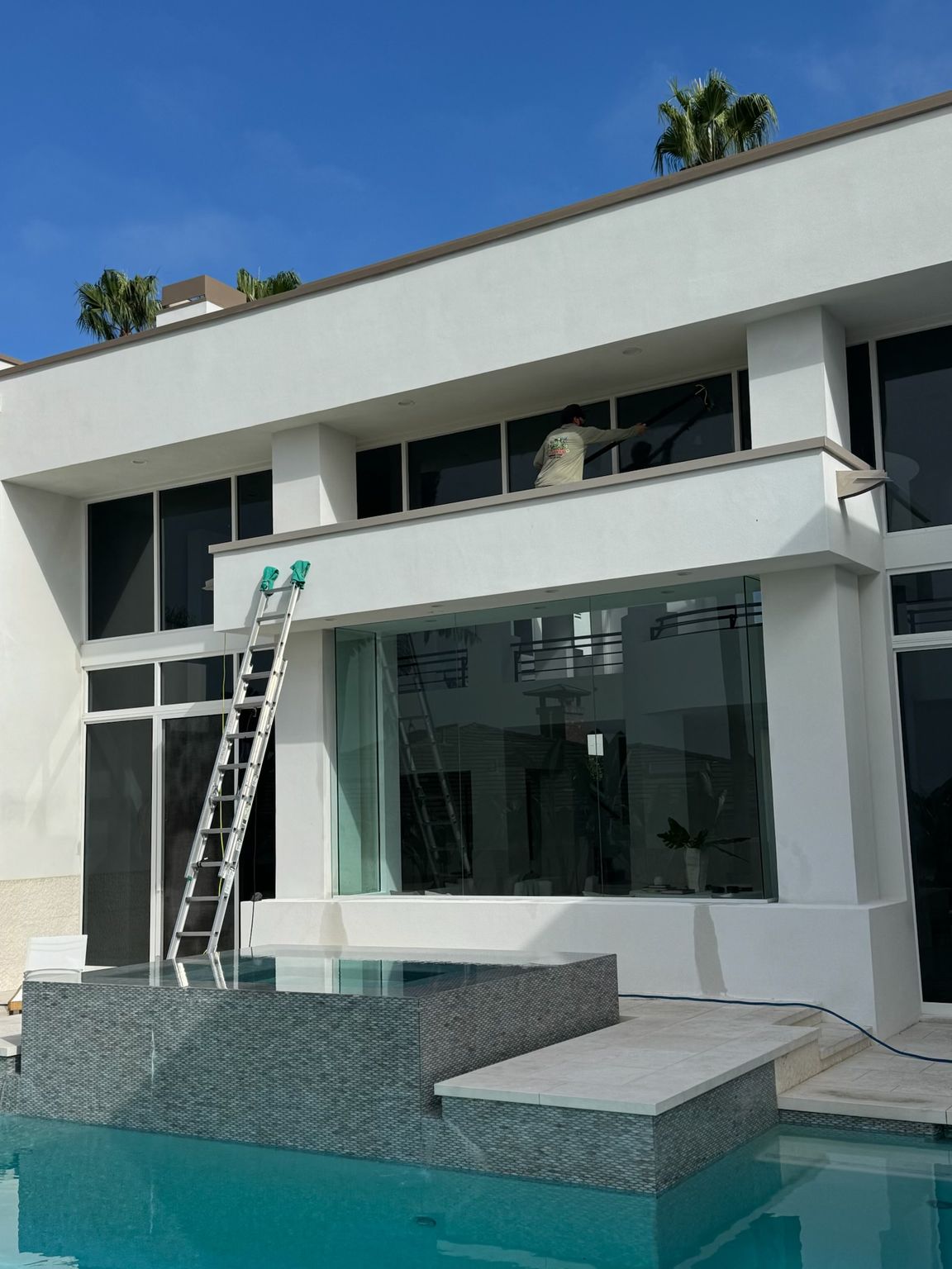 Modern white two-story house with pool, balcony, and a ladder leaning against the upper floor.