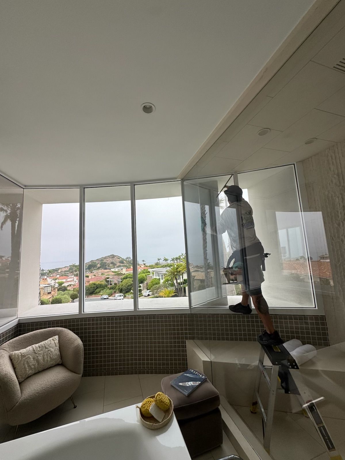 Worker cleaning windows in a bright living room with a bay view.