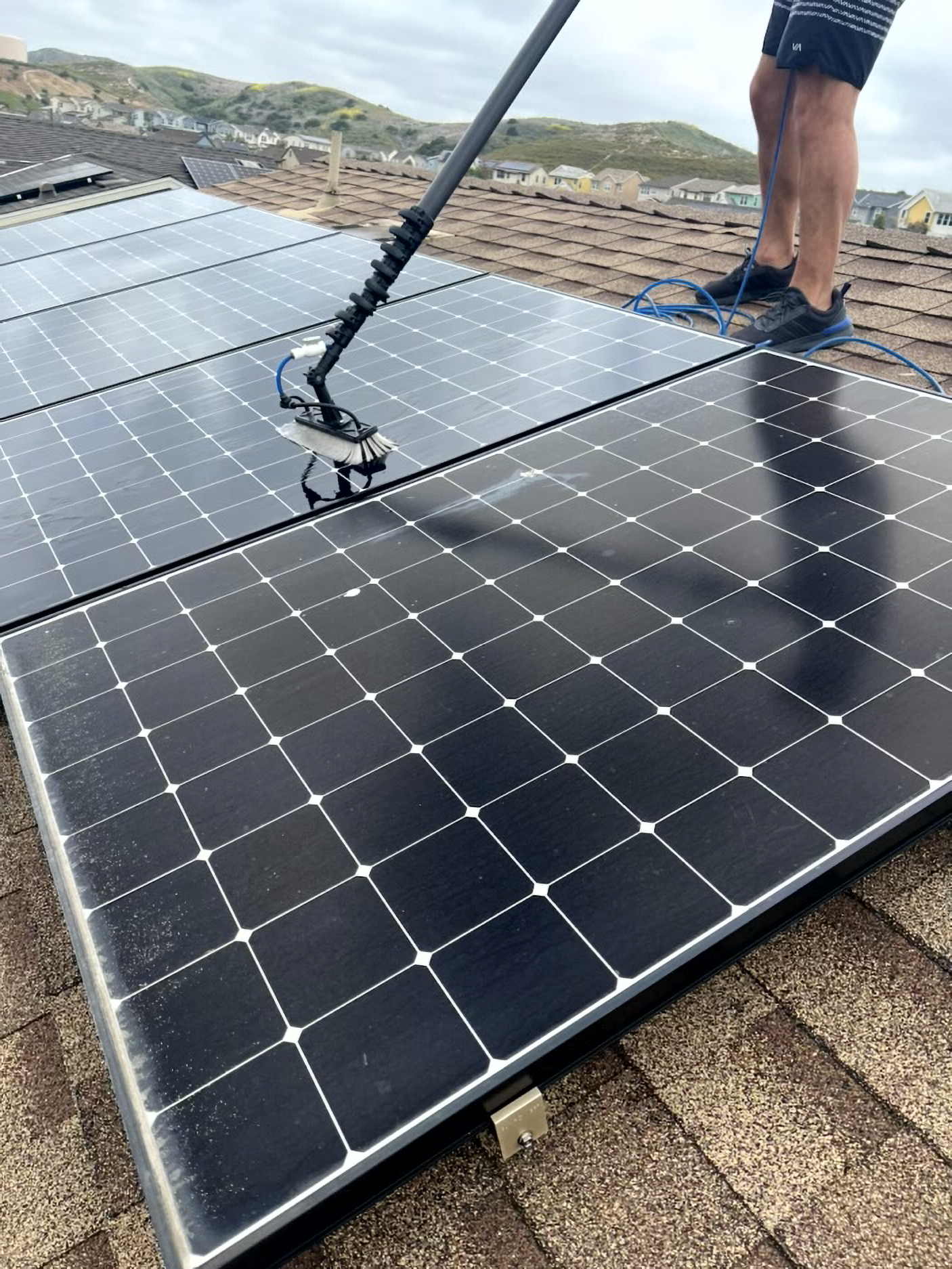 Worker cleaning solar panels on a rooftop with a long-handled brush