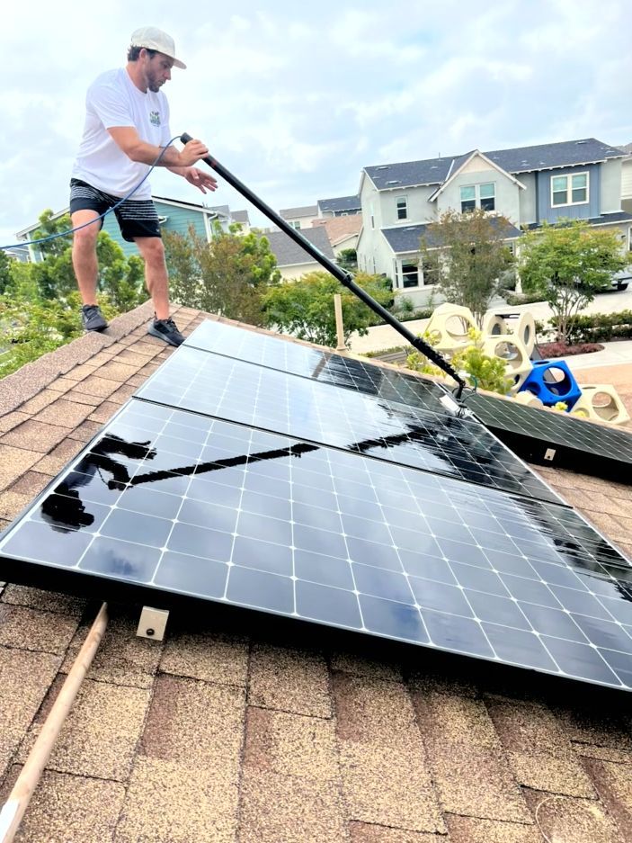 Worker cleaning solar panels on a rooftop with a water spray wand