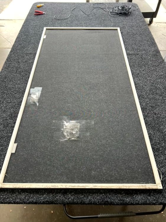 Black carpeted board with a white rectangular frame on a worktable, with small tape patches and tools nearby