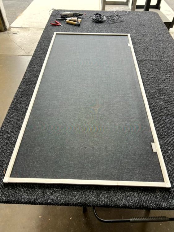 Large screen door frame with mesh laid on a carpeted floor, with tools at the top edge.