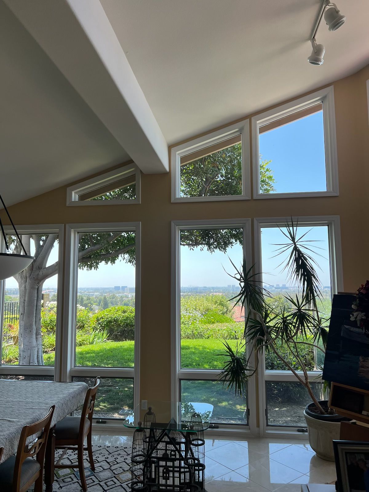 Bright living room with floor-to-ceiling windows overlooking a sunny garden and distant water.