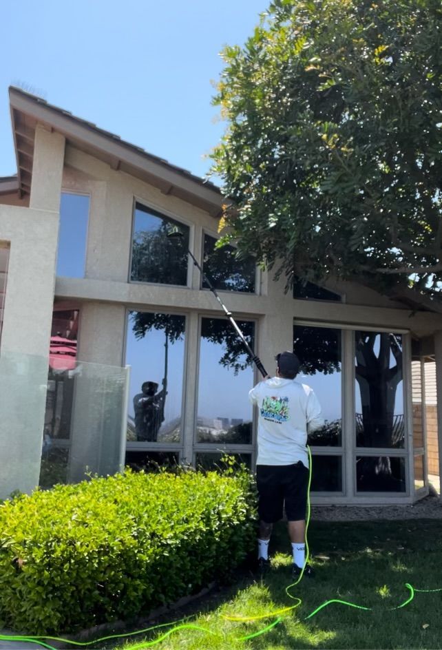Person watering shrubs outside a two-story house on a sunny day