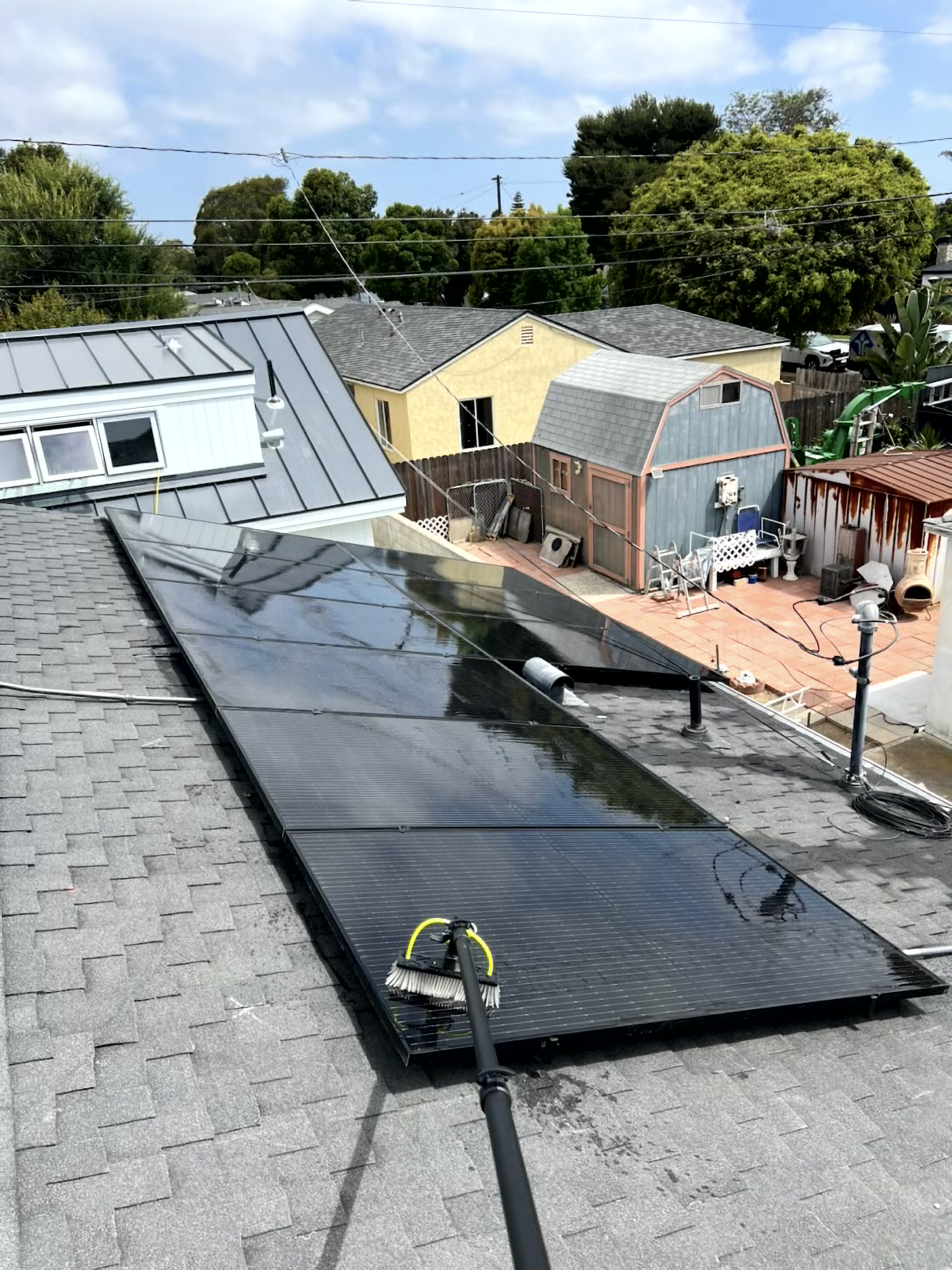 Rooftop solar water-heating panels on a gray shingled roof, with houses and trees in the background