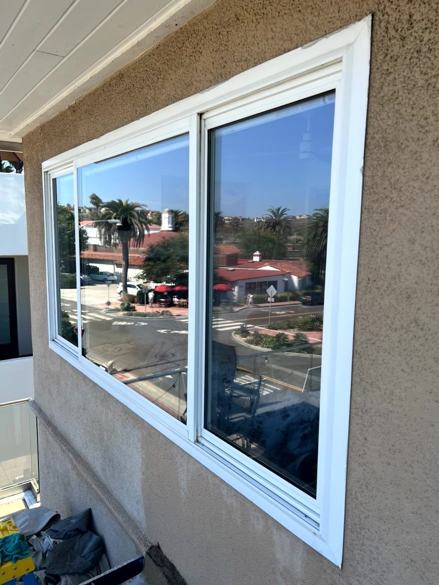 Corner of a beige stucco building with a large white-trimmed window reflecting the street and sky