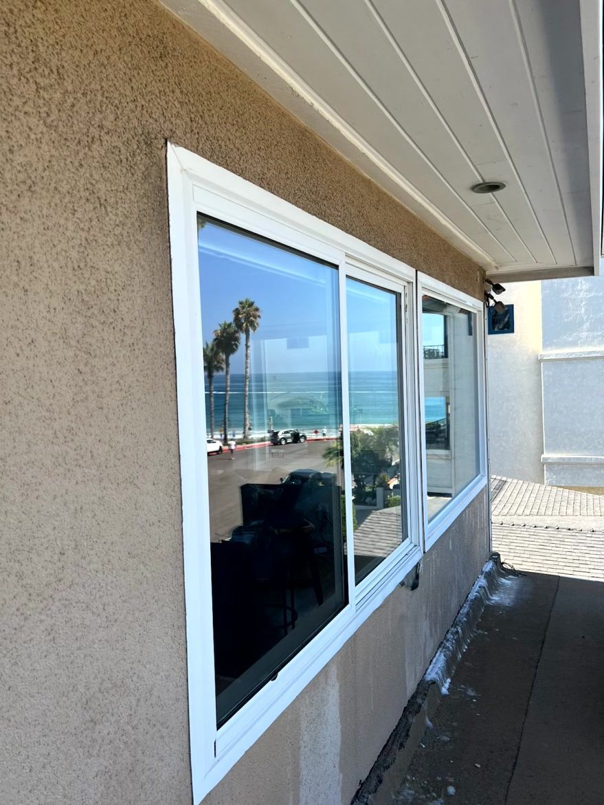 Side of a beige building with white-framed windows overlooking the ocean and beach.