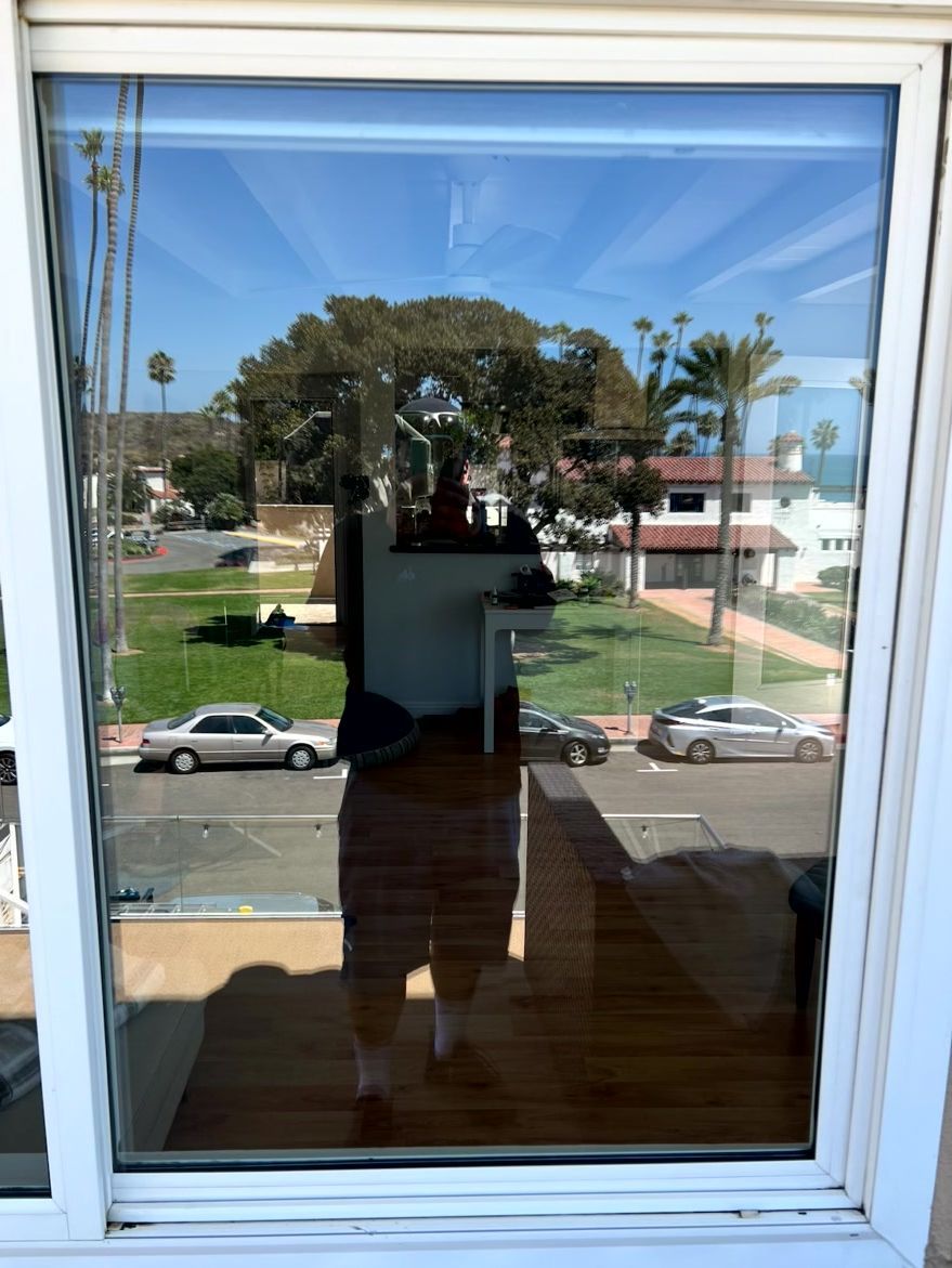 Person’s reflection in a window overlooking a street with cars, trees, and buildings.