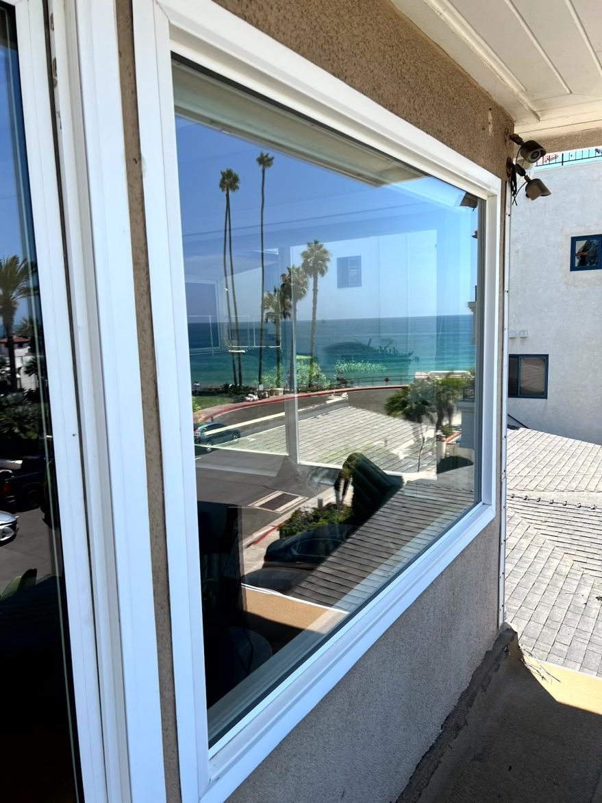 Ocean view reflected in a window beside a sunlit patio and white building