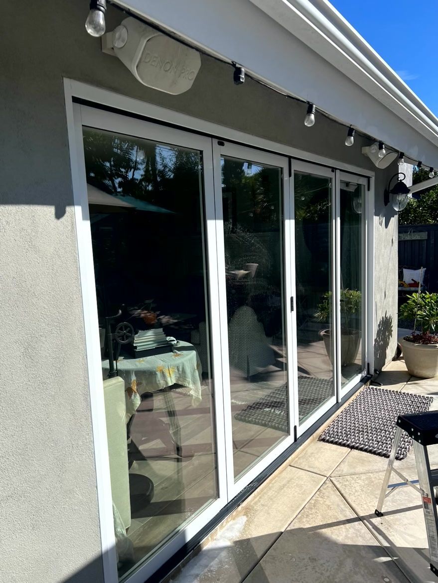 Sliding glass doors on a patio beside a house, with string lights and outdoor seating visible inside.