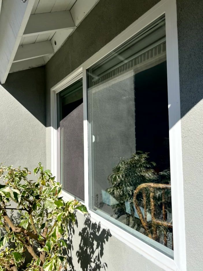 Exterior of a house with a large window and sliding glass door beside potted plants and a shaded patio