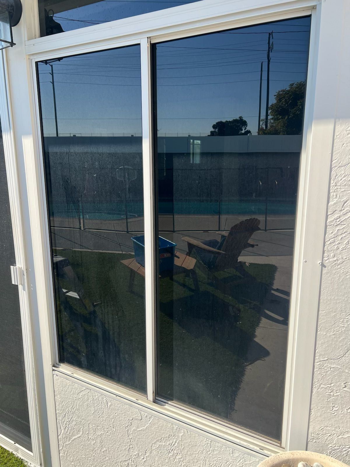 Sliding glass patio door reflecting a patio chair and ocean view at sunset
