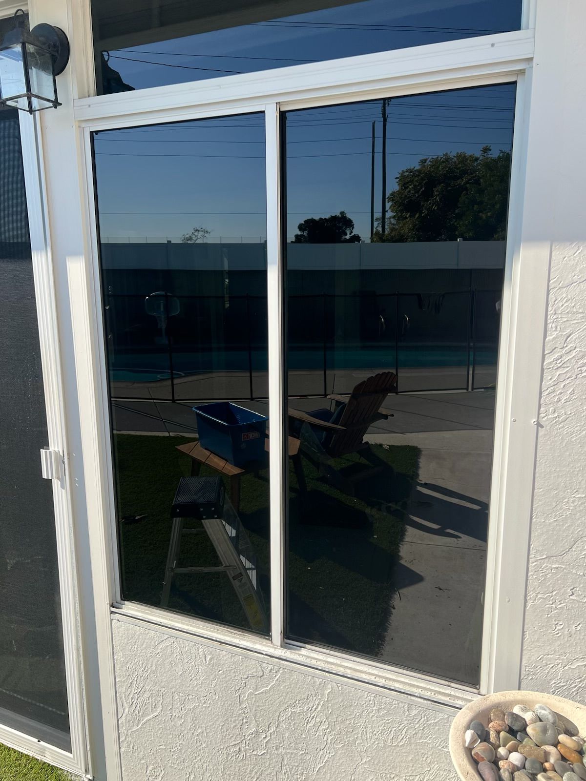 Sliding glass door with white frame reflecting outdoor seating and a pool area