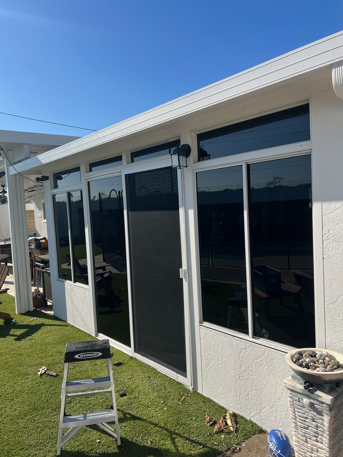 Backyard patio with sliding glass doors, a step ladder, and a white planter in sunlight