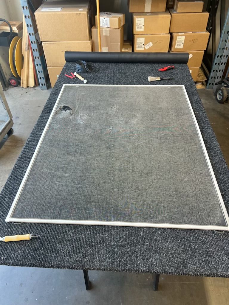 Gray carpet sample on a black worktable in a warehouse, with boxes and tools in the background