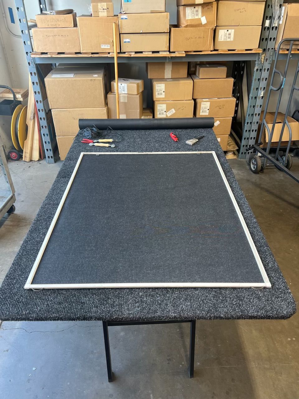 Black tabletop display board in a warehouse, with boxes stacked on shelves in the background.