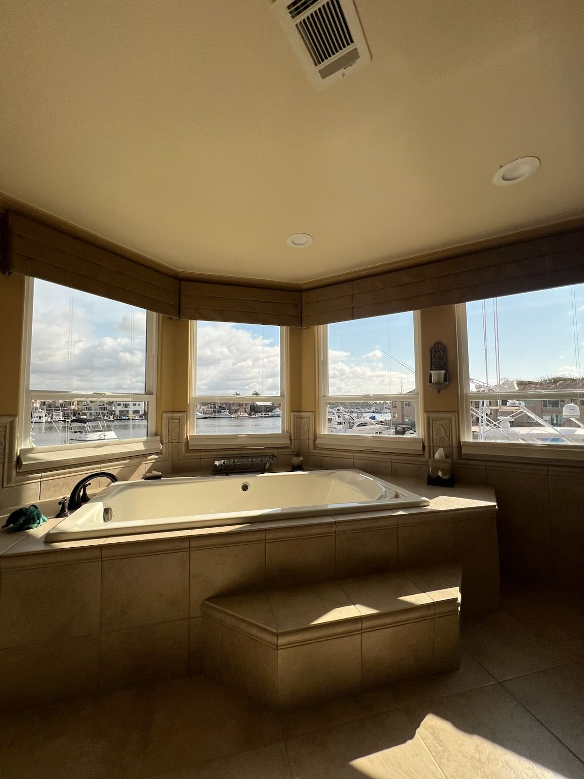 Corner bathtub room with large windows and harbor view, beige walls, and a cushioned bench