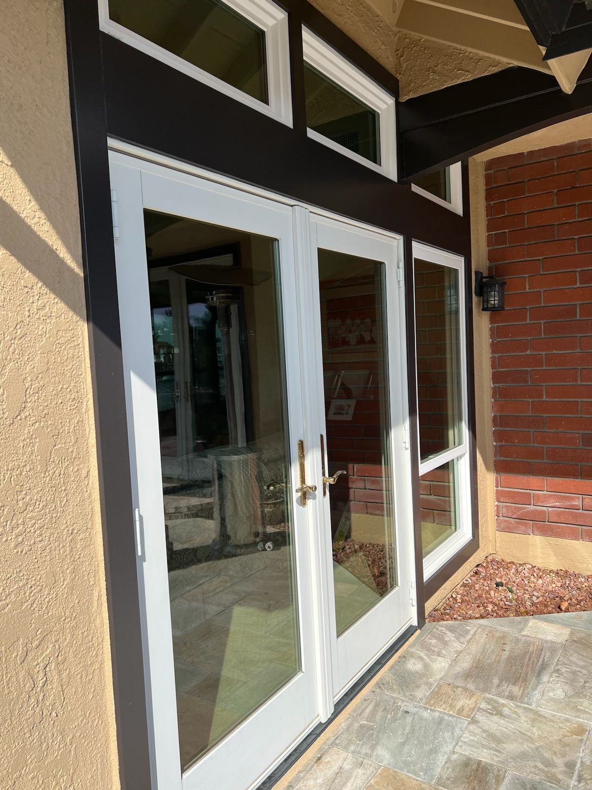Glass double doors at a building entrance with white frames, brick wall, and stone walkway