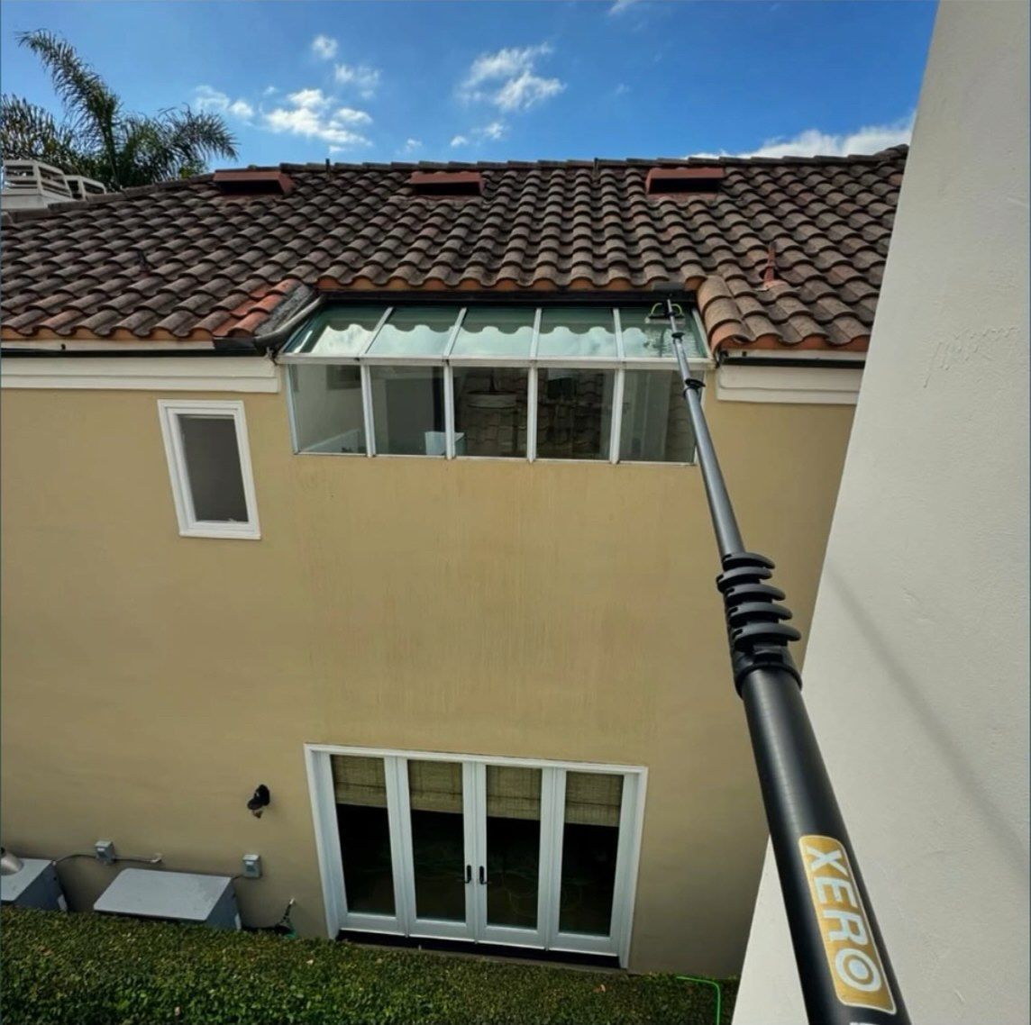View from a balcony of a tan townhouse with a tiled roof, windows, and a long pole reaching toward the upstairs window