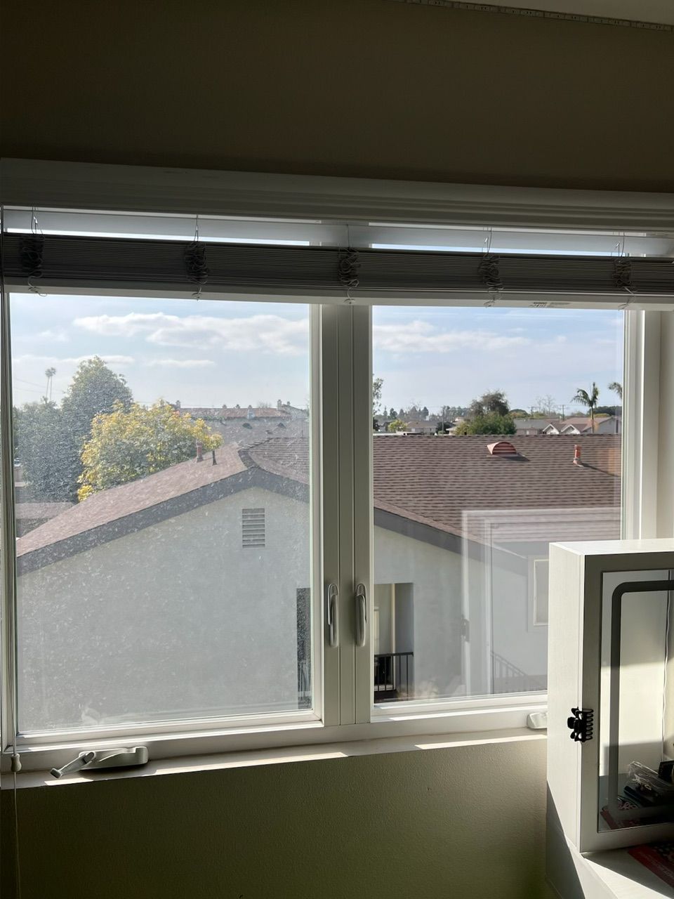 View through a bedroom window of neighboring rooftops and trees on a clear day