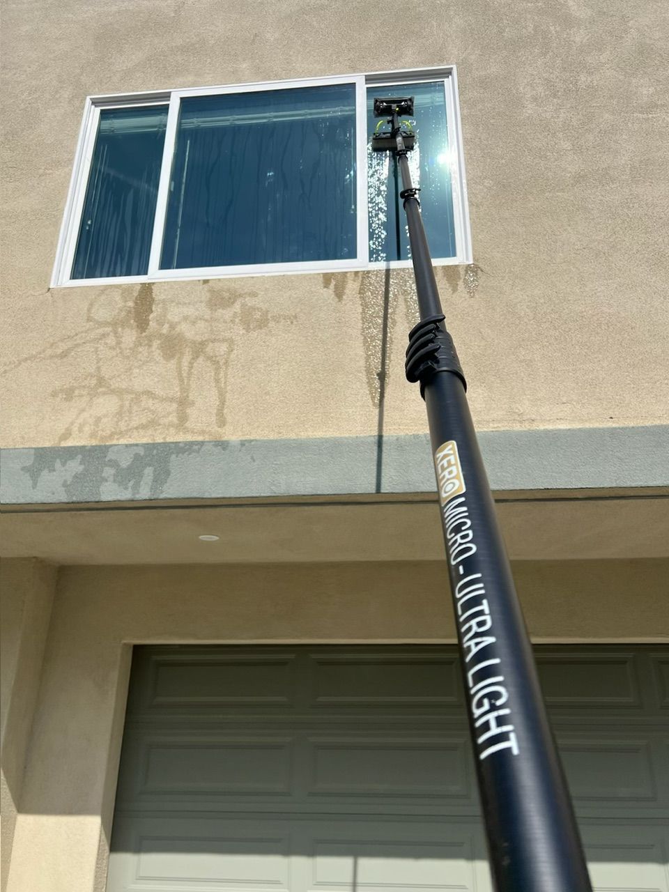 A window on a stucco building being cleaned with a long black pole labeled “VANCA TILATIGHT.”