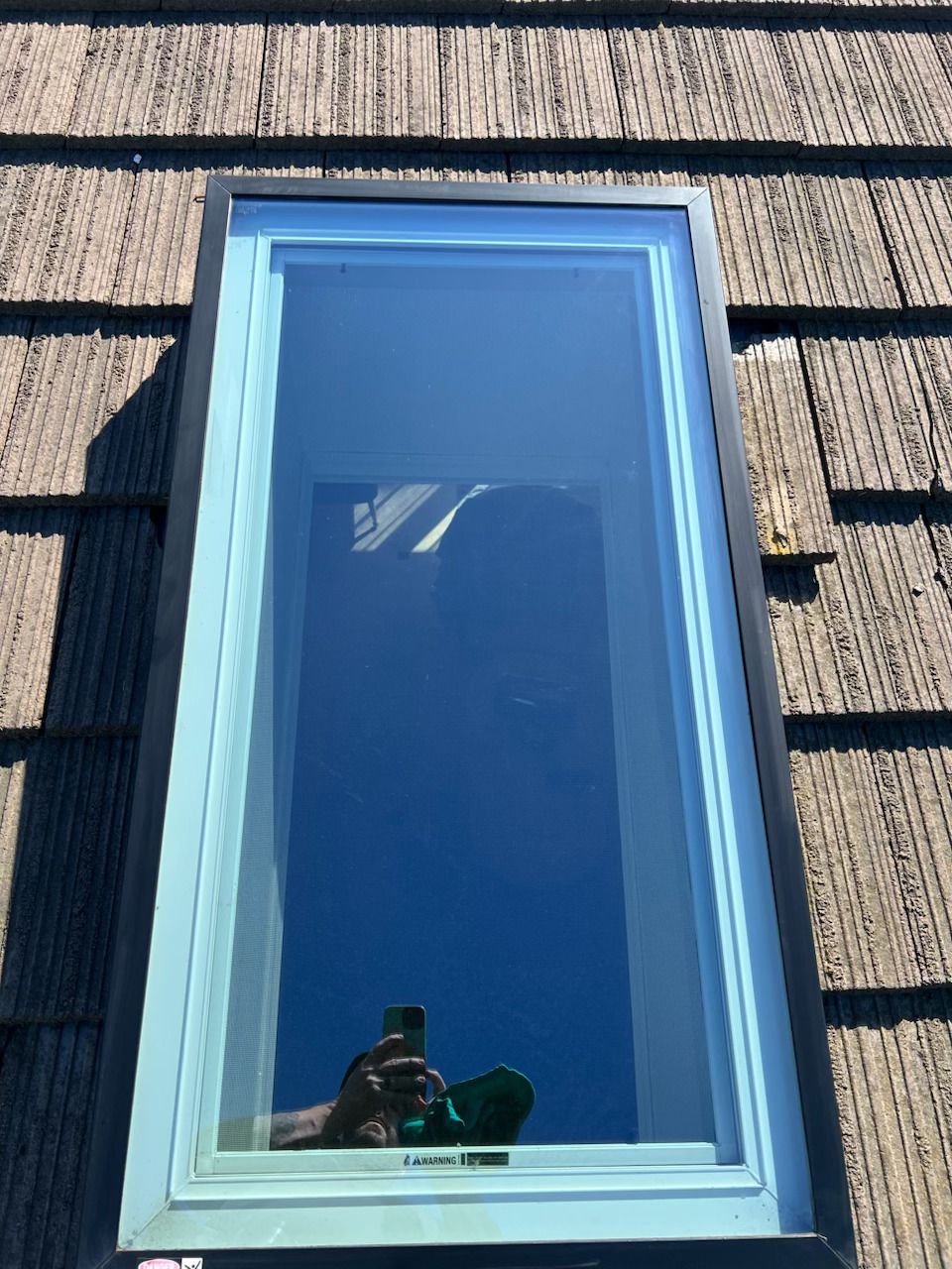 Blue-framed window in gray siding, reflecting the sky and a photographer at the bottom edge
