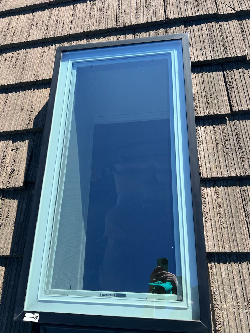 Blue-framed window in a textured wall, reflecting the sky and a photographer near the bottom.