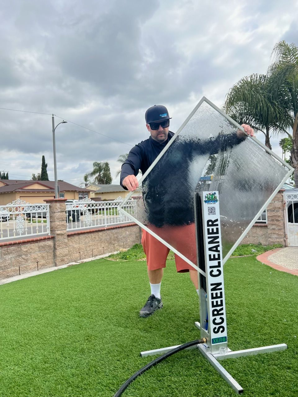 Man cleaning a window with a screen cleaner tool outdoors on a cloudy day