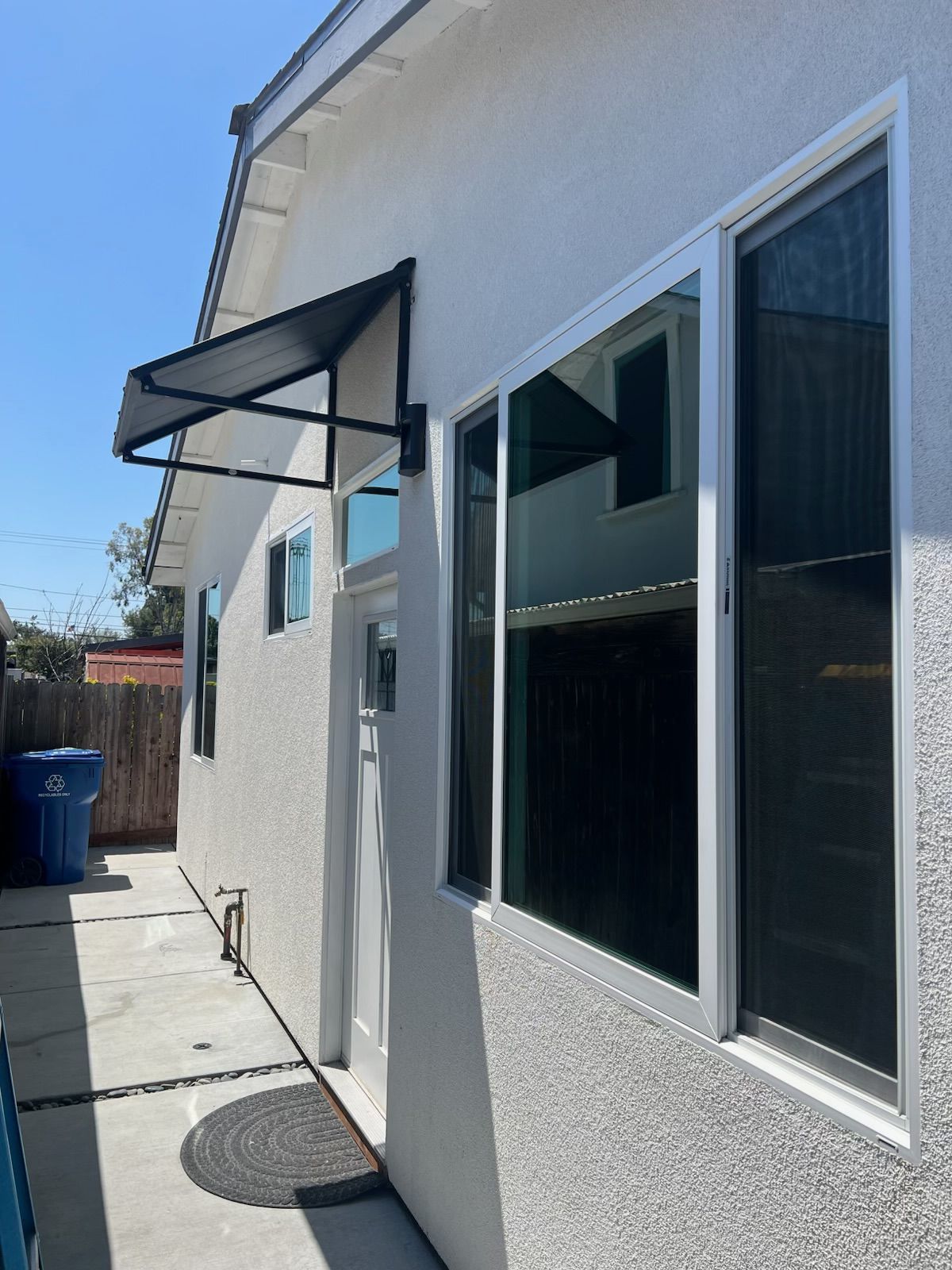 Side view of a beige building with dark-tinted windows, a door awning, and a concrete walkway.