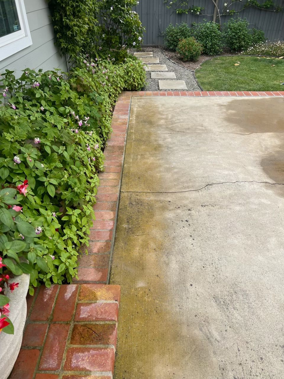 Brick-edged driveway beside a lush garden and stone path leading to a house