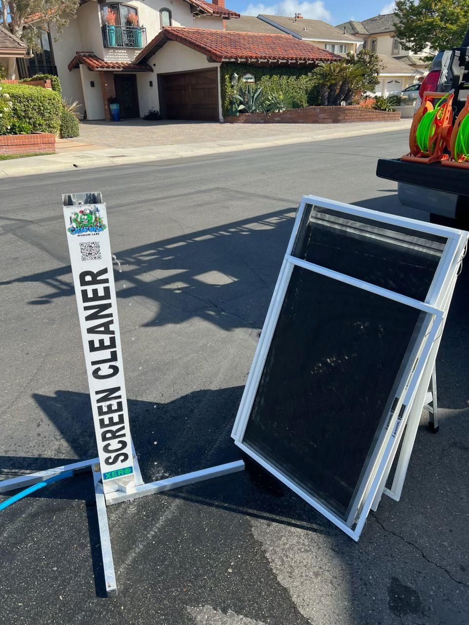 Street sign reading “SCREEN CLEANER” beside a tilted black display frame on a residential street.