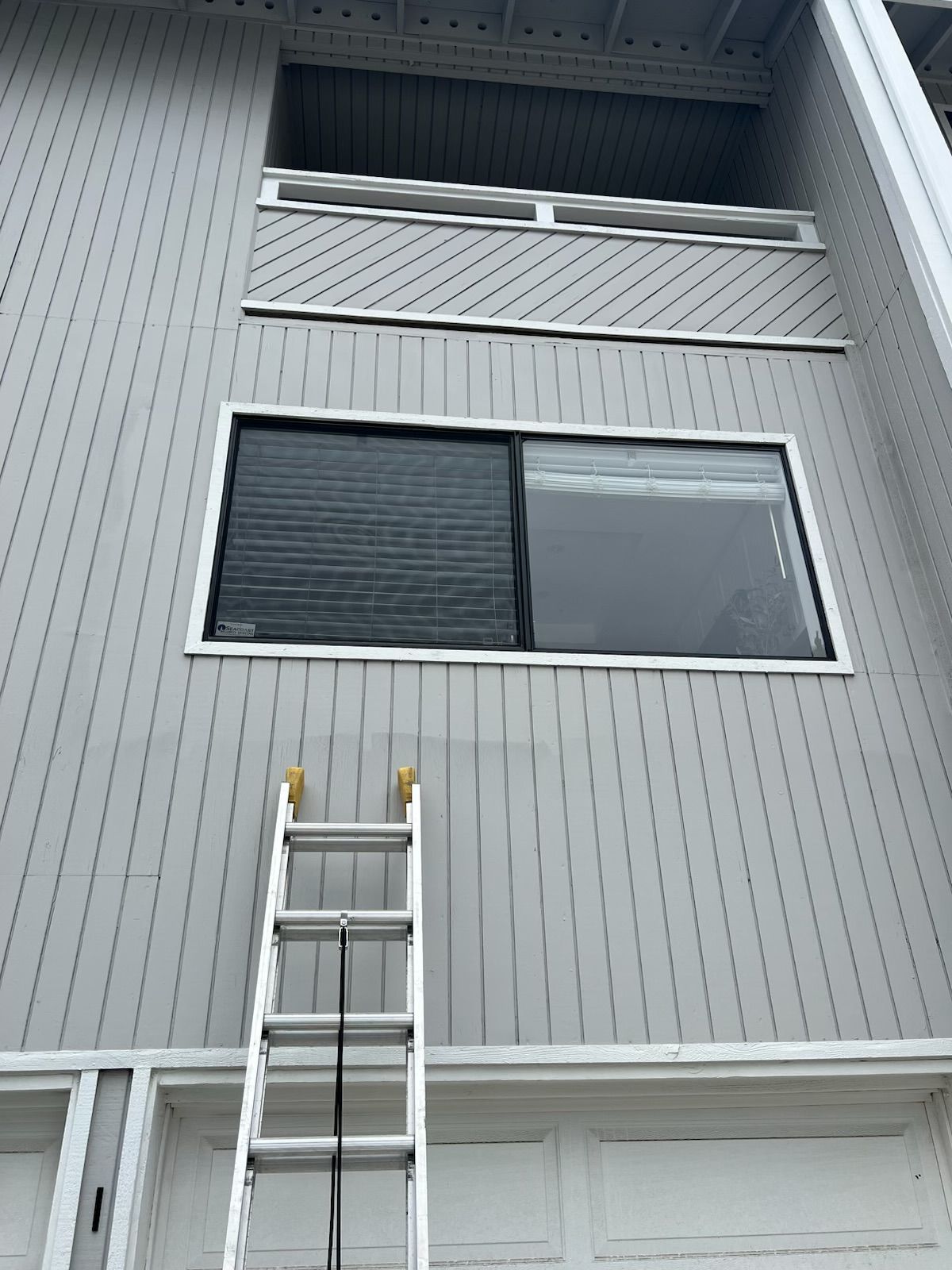 Aluminum ladder leaning against a gray building beneath a window.