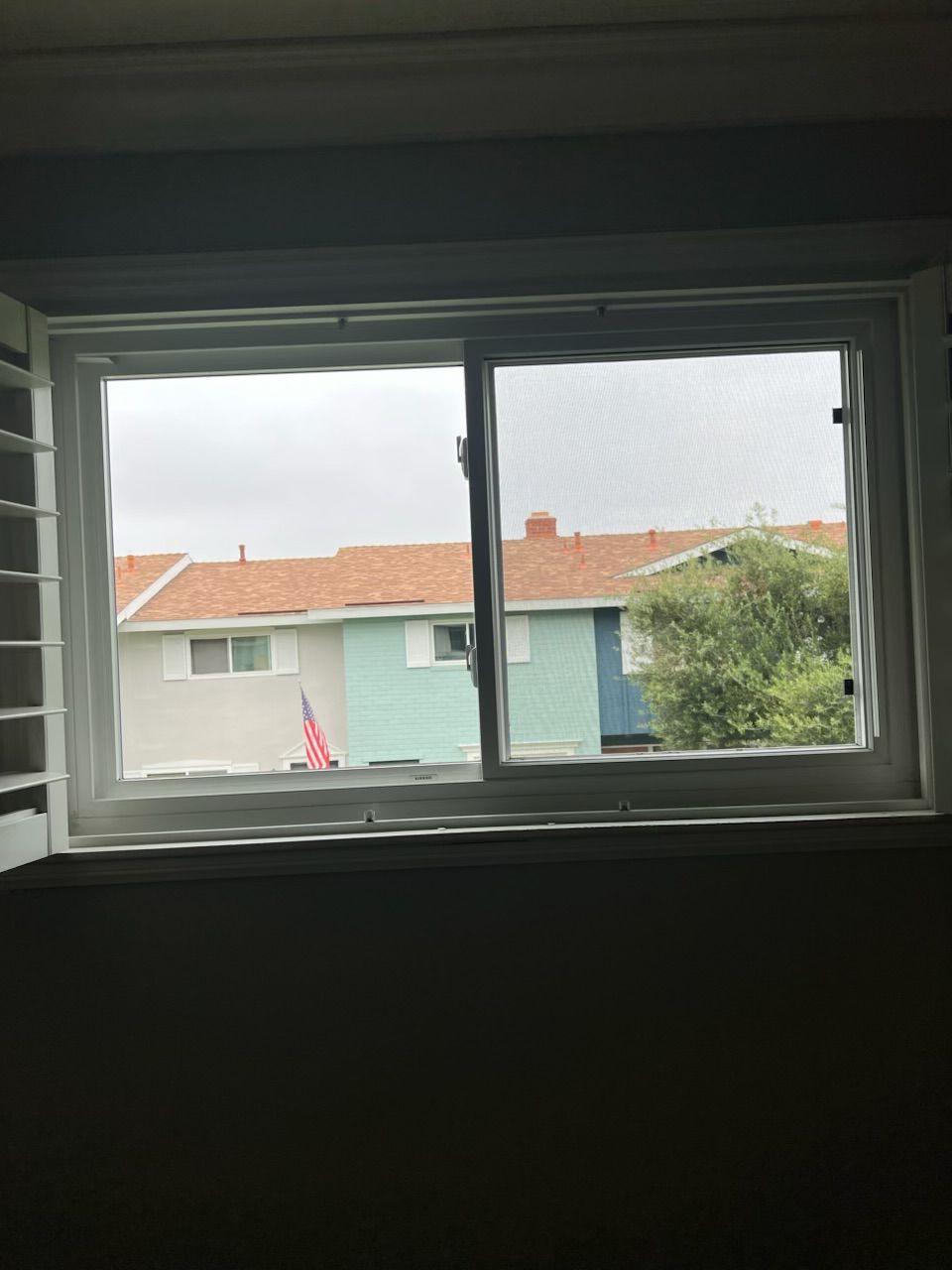 View through a white-framed window to neighboring houses with red roofs and a tree outside.