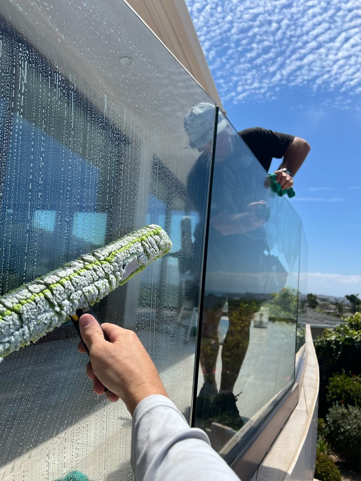Worker cleaning a glass building facade with a squeegee under a blue sky
