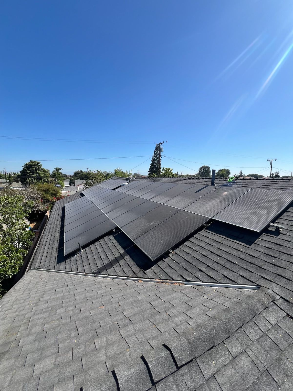 Roof with damaged shingles and loose solar panels under a clear blue sky
