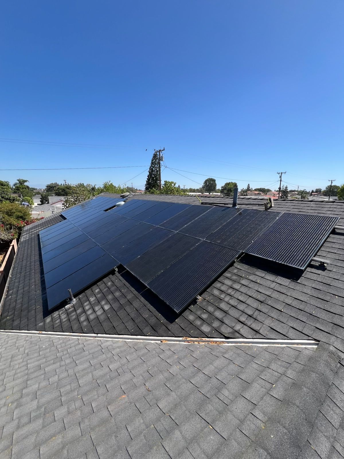Solar panels on a gray shingle roof under a clear blue sky.