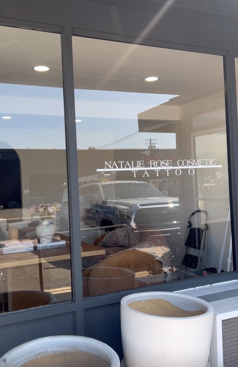 Office interior seen through glass doors, with desks, chairs, and a white planter in the foreground.