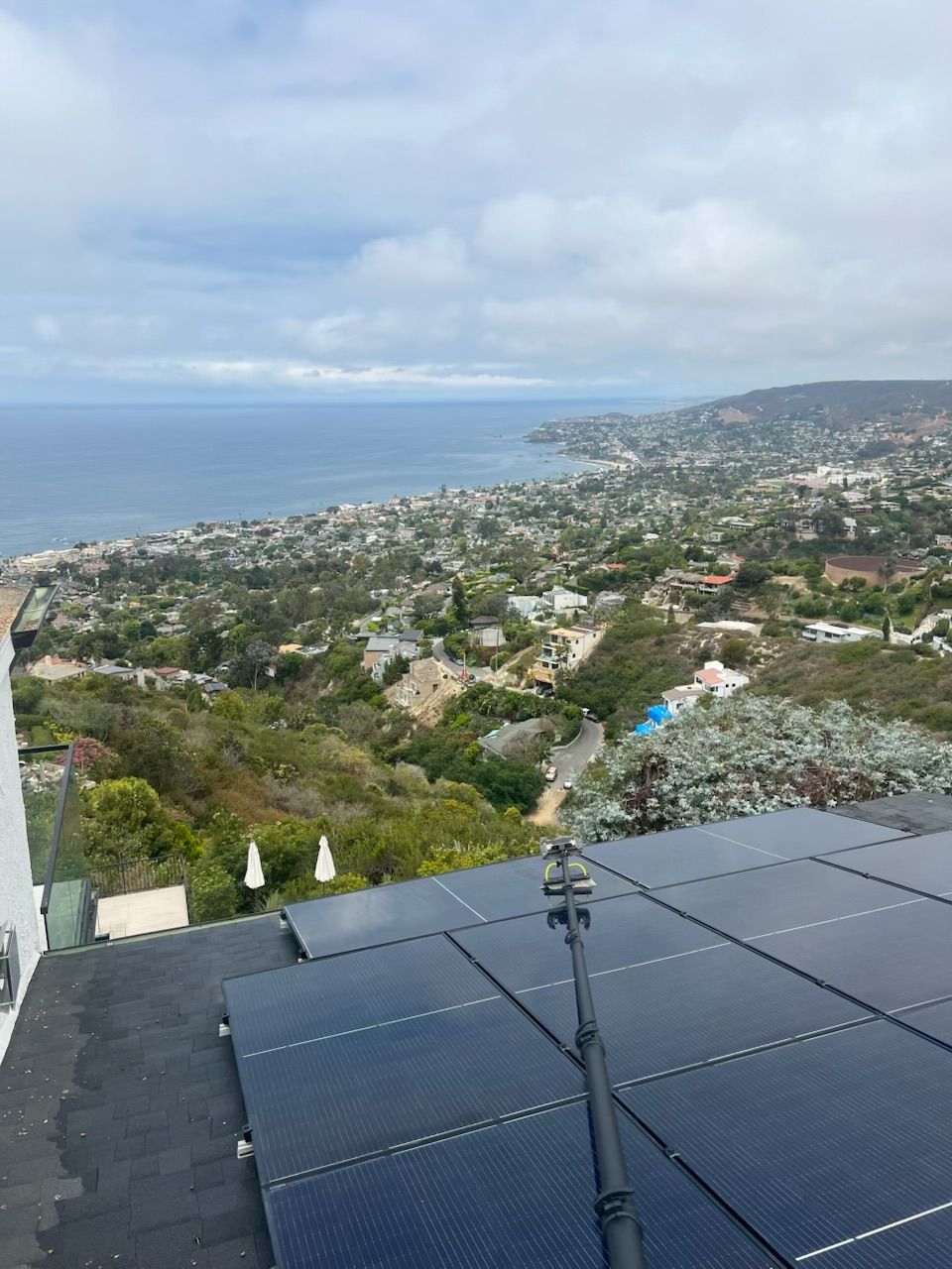 Rooftop solar panels overlooking a coastal hillside town and ocean under cloudy skies